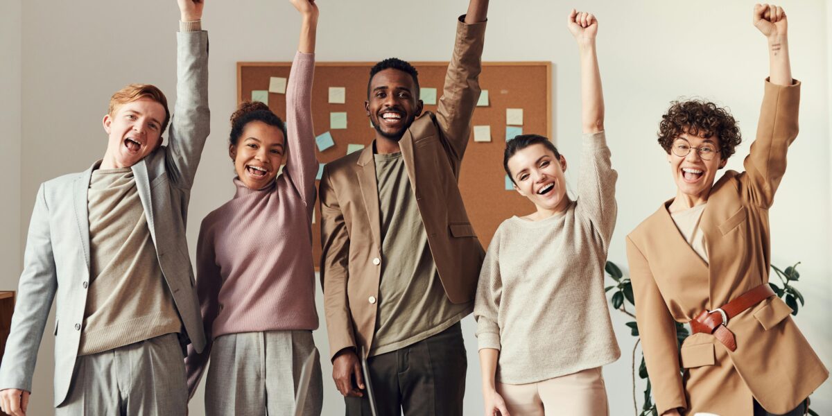 A diverse team celebrating success with raised hands in a modern office setting.