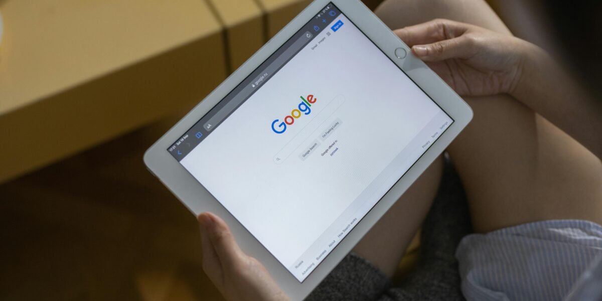 Close-up of hands holding a tablet showing the Google search page.